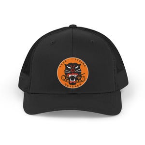 Peut inclure: Casquette de camionneur noire avec un dos en filet et une visière incurvée. L'avant présente un écusson circulaire avec une tête de panthère noire, un char et les mots "SEEK STRIKE DESTROY".