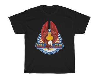 Pode incluir: Camiseta preta com um gráfico de uma águia vermelha, branca e azul com as palavras "Fall Guy Stuntman Assoc." em um círculo.
