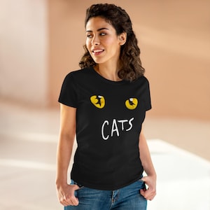 Puede incluir: Camiseta negra con un diseño temático de gatos. La camiseta tiene ojos de gato amarillos encima de la palabra "CATS" en blanco, creando un aspecto lúdico y reconocible. La camiseta es de estilo cuello redondo clásico.