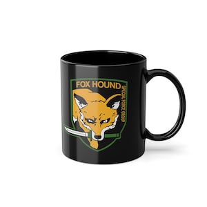 May include: Black ceramic mug with a graphic of a fox head with a knife in its mouth. The graphic is surrounded by a green shield with the text "FOX HOUND SPECIAL FORCE GROUP" in yellow.