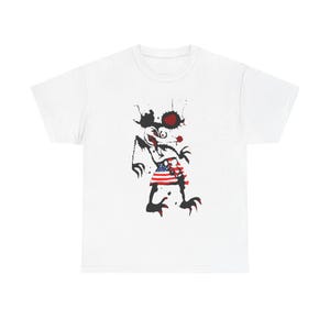 May include: White t-shirt featuring a black and white illustration of a cartoon character wearing a red, white and blue skirt. The character has a large, red nose and a surprised expression.