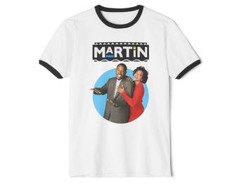 May include: White ringer t-shirt with black trim. The shirt has a graphic of two people in a blue circle, with the word "MARTIN" above them. The graphic is in a retro style, with a black, white, blue, and yellow colour scheme.
