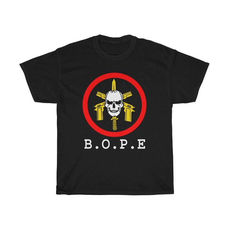 Puede incluir: Camiseta negra con un emblema central que presenta una calavera, pistolas cruzadas y una espada, todo dentro de un c&iacute;rculo rojo. El texto blanco "B.O.P.E" est&aacute; impreso debajo.