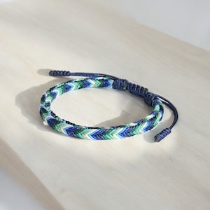 May include: A blue, green and white braided friendship bracelet with a dark blue adjustable closure.