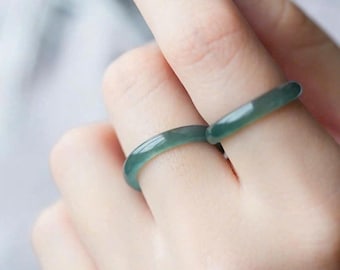May include: Two smooth, polished jade rings with a translucent, light green hue. The bands are thin and rounded, featuring a consistent, solid color throughout. These circular rings are worn on two separate fingers, showcasing their simple, polished finish.