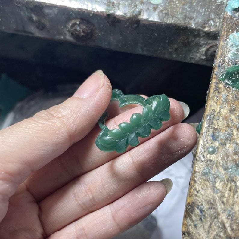 May include: A dark green wax ring model featuring a detailed carved leaf and floral pattern. The ring is semi-translucent and shows intricate botanical textures across the band, designed for the lost-wax casting process in jewelry making.