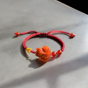 Puede incluir: Pulsera de cuerda roja con un dije de pez de piedra roja tallada y cuentas rojas.