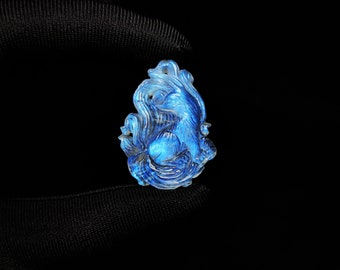 Op de afbeelding: Een blauwe en witte gegraveerde labradorit hanger met een ontwerp van een mythisch wezen.
