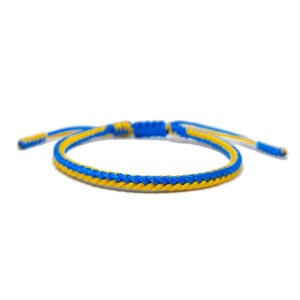 Könnte beinhalten: Ein geflochtenes Freundschaftsarmband in Blau und Gelb. Das Armband besteht aus zwei Schnüren, einer blauen und einer gelben, die miteinander geflochten sind.