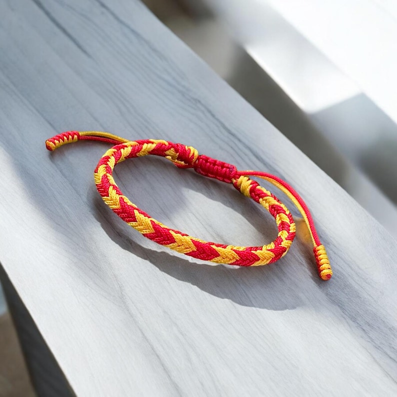 May include: A red and yellow braided friendship bracelet with a knot at each end.
