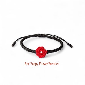 May include: A black string bracelet with a red poppy flower knot. Red Poppy Flower Bracelet.