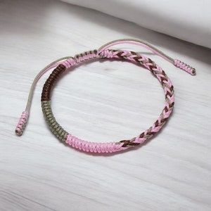 Könnte beinhalten: Ein geflochtenes Freundschaftsarmband in Pink und Braun mit einem geknoteten Verschluss.