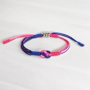 May include: A blue, pink, and white braided bracelet with a silver bead accent and a knotted design.