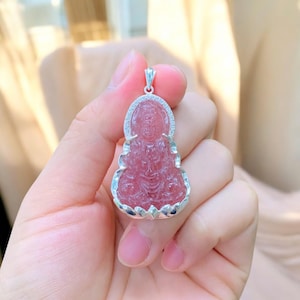 Peut inclure: Un pendentif en cristal rose avec une image sculptée de Bouddha, sertie dans un cadre argenté. Le pendentif est un bijou délicat et complexe.