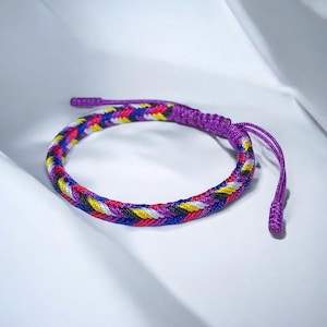 May include: A multi-colored braided bracelet with purple, red, white, yellow, and black threads. The bracelet has a knot at each end.