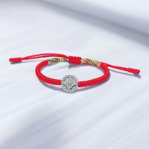 Peut inclure: Bracelet en cordon rouge avec un charme argenté représentant un mandala détaillé.