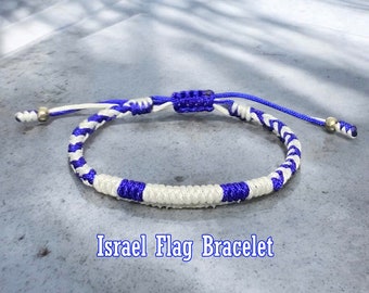 May include: A white and blue braided bracelet with a knot at the top. The bracelet is made of two colors of string, white and blue, and is braided in a pattern that resembles the Israeli flag. The text "Israel Flag Bracelet" is written below the bracelet.