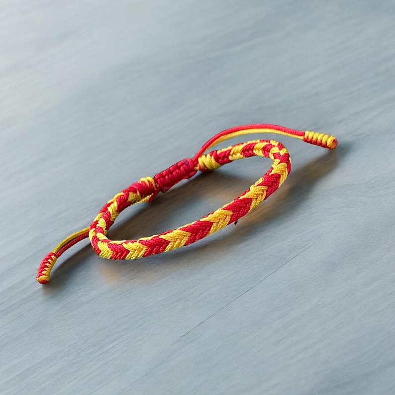May include: A red and yellow braided friendship bracelet. The bracelet is made of two strands of cord that are woven together in a simple pattern.