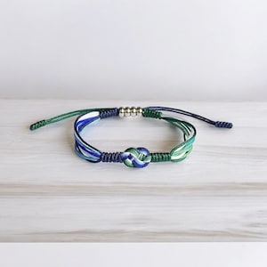 Puede incluir: Un brazalete trenzado azul, verde y blanco con un acento de cuentas plateadas y un cierre anudado.
