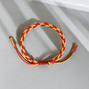 May include: A red and yellow braided friendship bracelet with a knot at the end.