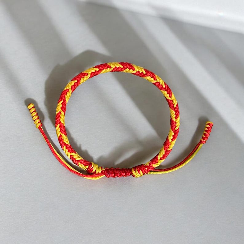 May include: A red and yellow braided friendship bracelet with a knot at the end.