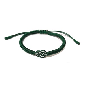 May include: A green braided bracelet with a white knot in the center.
