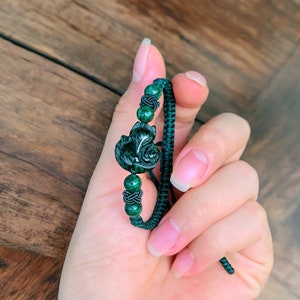 May include: A green jade bracelet with a carved fox charm and dark green beads. The bracelet is tied with a dark green cord.