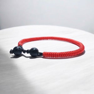 May include: Red string bracelet with two black beads, each with the number "2" engraved on them.