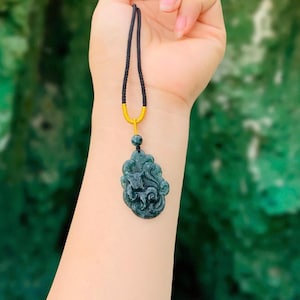 Op de afbeelding: Donkerblauwe hangerketting met een gebeeldhouwd ontwerp van een mythisch wezen. De hanger hangt aan een zwart koord met een goudkleurig accent. De ketting wordt getoond tegen een vage groene achtergrond.