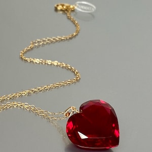 May include: A gold chain necklace with a large, red heart-shaped pendant.