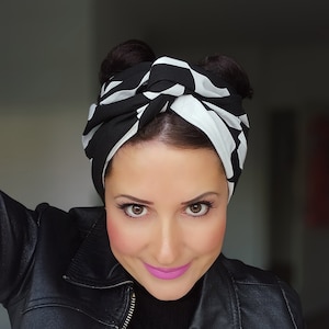 Könnte beinhalten: Ein schwarz-weiß gemustertes Turban-Stirnband. Der Stoff hat ein kühnes, geometrisches Design. Das Stirnband ist oben geknotet. Die Person trägt eine schwarze Lederjacke.