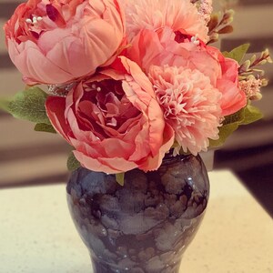 May include: A bouquet of pink peonies and carnations in a black and white marbled vase.