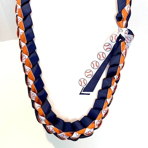 Puede incluir: Un collar de flores de cinta azul y naranja con un patrón de béisbol. El collar está hecho de dos cintas que están trenzadas juntas.