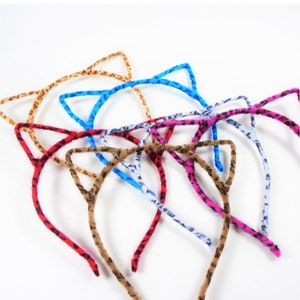 May include: A set of six colorful cat ear headbands. The headbands are made of a soft, fuzzy material and feature a leopard print design. The headbands are perfect for adding a touch of whimsy to any outfit.