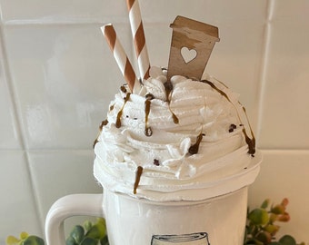 May include: A white ceramic mug topped with whipped cream, caramel drizzle, and chocolate sprinkles. Two brown and white striped straws and a wooden coffee cup cutout with a heart detail add to the decorative coffee theme.