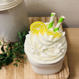 May include: A white ceramic cup filled with whipped cream, decorated with yellow lemon slices and green and white striped straws. A decorative lemon-themed dessert on a wooden surface.