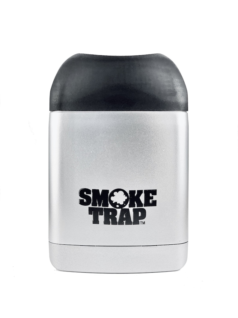 May include: A silver metal container with a black lid. The container has the words "SMOKE TRAP" printed on the front in black.