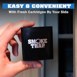 May include: A black square-shaped air freshener with the text "SMOKE TRAP" in white letters and a silver circle with a black smoke cloud inside.