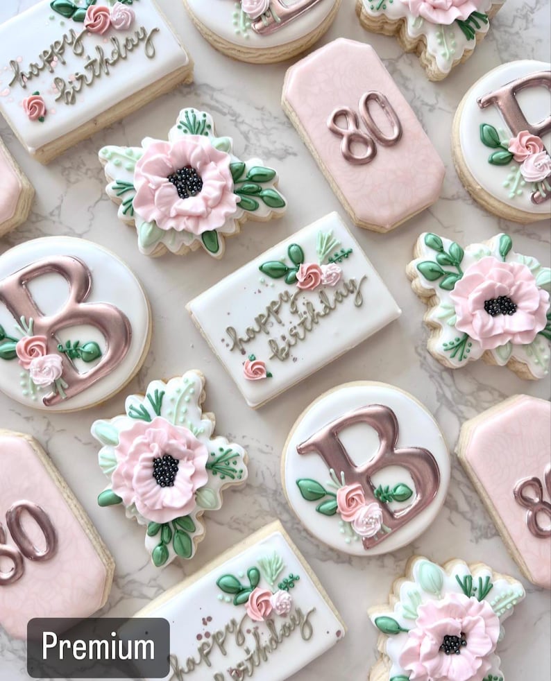 May include: A collection of decorated sugar cookies with pink and white icing. The cookies feature floral designs, the letter "B", and the number "80". Some cookies have the text "Happy Birthday" written on them.