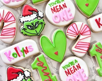 Pode incluir: Um conjunto de biscoitos de açúcar decorados com um personagem verde do Grinch, bengalas de doces, corações e as palavras "You're a Mean One" e "Kollyns".