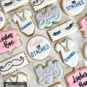 May include: A collection of decorated sugar cookies with various designs, including eyelashes, mustaches, baby onesies, and the words "Lashes or Staches" and "Baby".