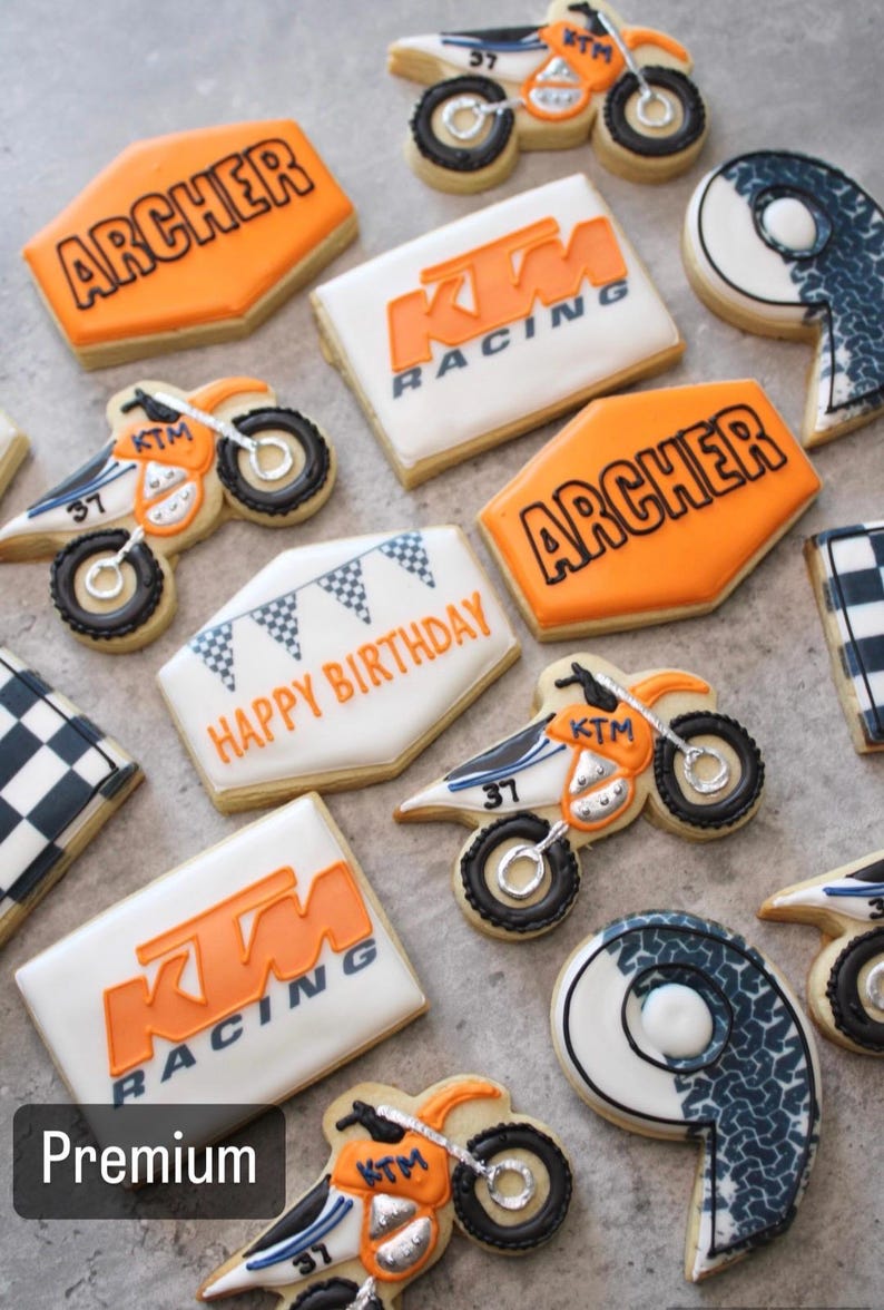 Pu&ograve; includere: Una collezione di biscotti di zucchero decorati con un tema di motocross. I biscotti sono decorati con glassa arancione, bianca e nera. I biscotti presentano le parole "KTM Racing", "Archer" e "Buon compleanno".