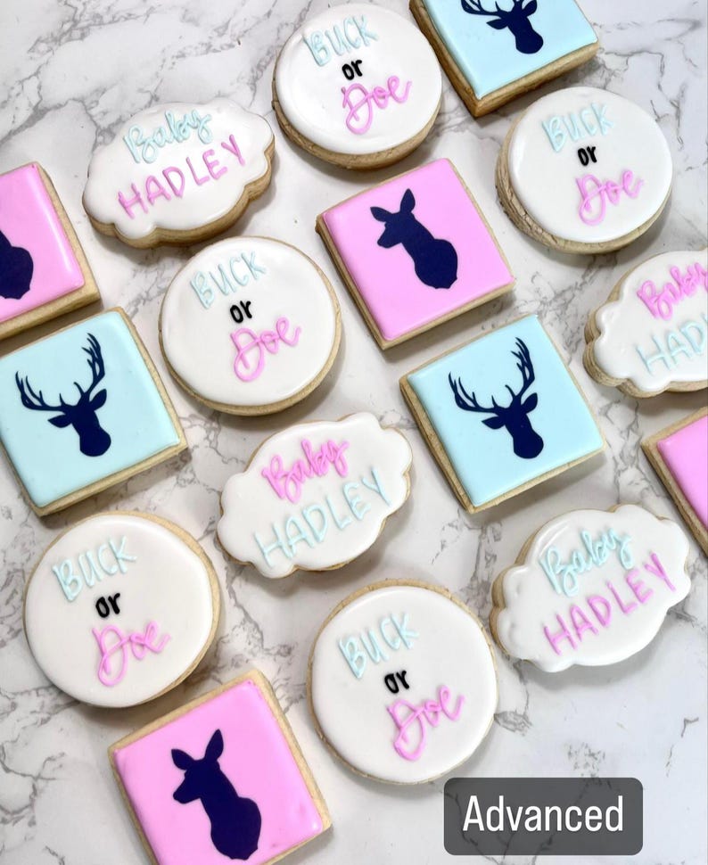 May include: A collection of decorated sugar cookies with various designs, including a deer silhouette, the words "Baby Hadley", and "Buck or Doe". The cookies are decorated with pink, blue, and white icing.