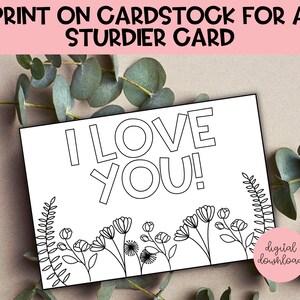 May include: Printable coloring page featuring the words "I love you!" in bold, outlined letters. The design includes a border of simple flowers and leaves.