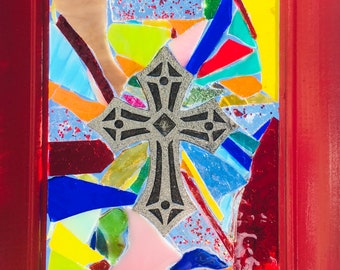 May include: A framed mosaic artwork featuring a black cross with a silver-grey background. The mosaic is made of colorful glass pieces in shades of red, blue, yellow, green, and pink.