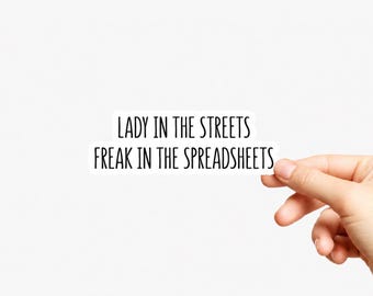 May include: A white rectangular sticker with black sans-serif text that reads LADY IN THE STREETS FREAK IN THE SPREADSHEETS. The sticker has a clean die-cut edge and features a simple, bold typography style suitable for application on various surfaces.