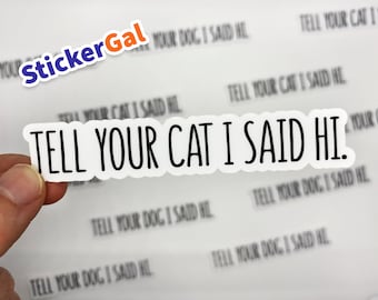 May include: A white die-cut vinyl sticker featuring the black text "TELL YOUR CAT I SAID HI." in a clean, sans-serif font. The sticker has a thin white border and is held against a sheet containing multiple identical stickers with the same text.