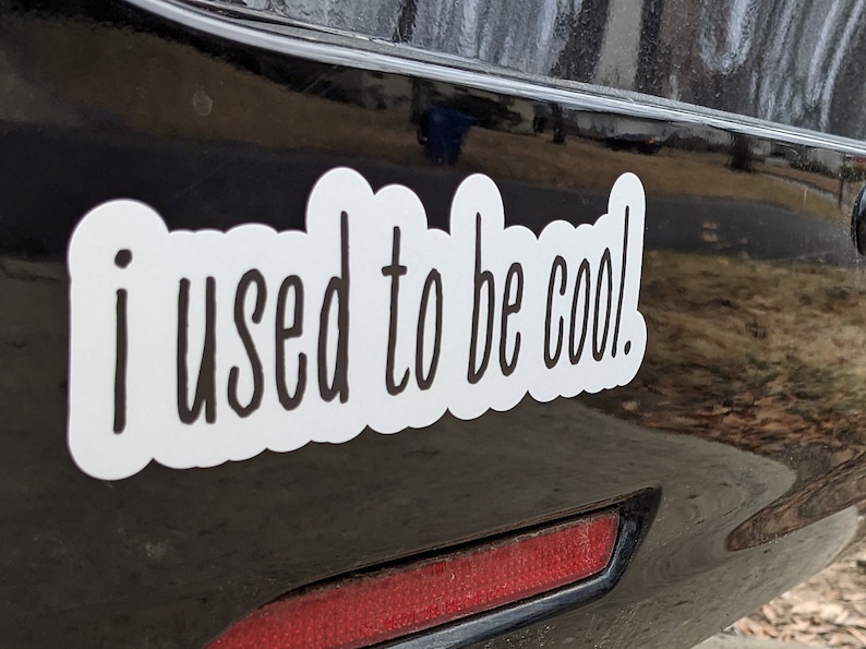 May include: A white vinyl decal with a black scalloped border and the black text "i used to be cool." in a handwritten font. The sticker is applied to a smooth, dark, reflective surface, featuring a clean, die-cut shape around the lettering.