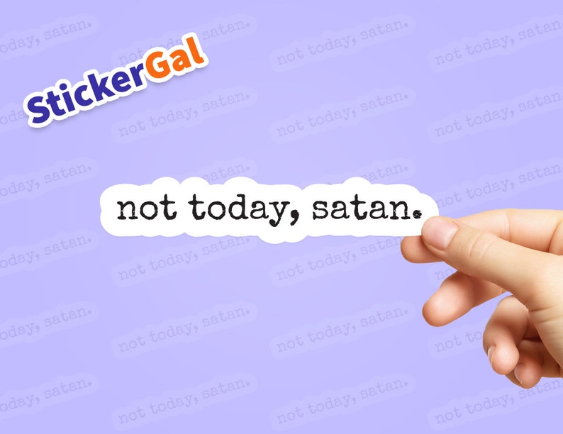 May include: A white sticker with the text "not today, satan." printed in black typewriter font. The sticker is being held by a hand against a light purple background with the text "not today, satan." repeated in a smaller font.