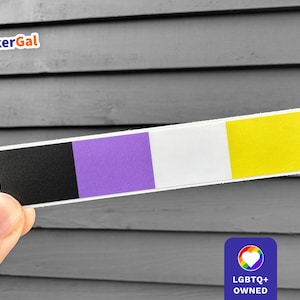 May include: A rectangular sticker with the non-binary pride flag colors: black, purple, white, and yellow. The sticker is held in front of a gray wooden background. The sticker has the text "StickerGal" at the top left.